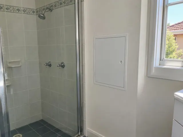 Neat access panel beside a shower in a tiled bathroom with a window and dry wall in Rydalmere